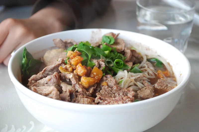 Глубокая миска с тайским супом с лапшой, мясными шариками и зеленью